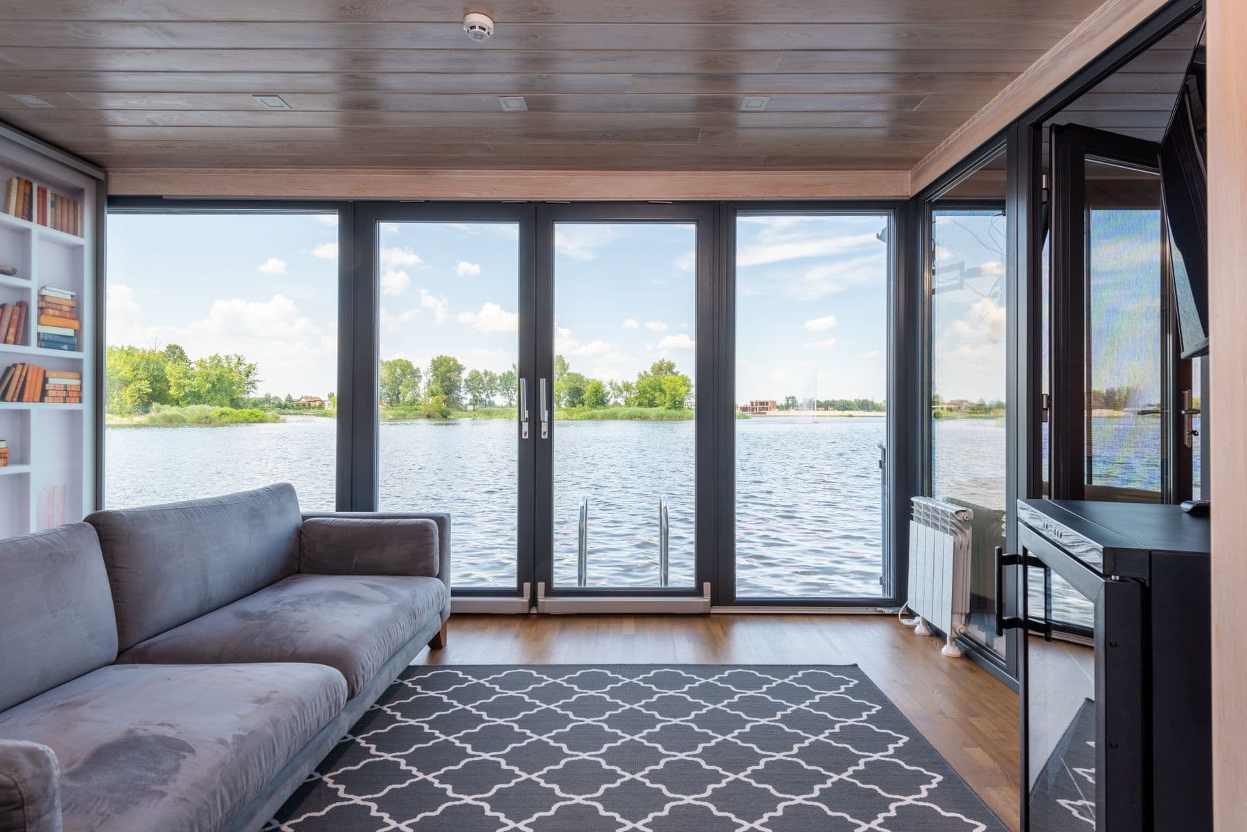 Salón con carpintería oscura y grandes puertas acristaladas que dan a un lago